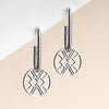 Pair of silver earrings with geometric designs on a beige and white background