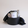 Black gift box with a candle labeled 'Wild Sage' and a small stack of stones on a light background